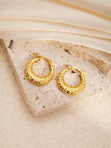 Hammered gold titanium steel hoop earrings on stone and silk fabric display