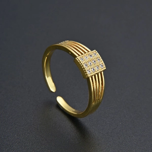 Dettaglio anello dorato con zirconi quadrati e fascia con texture a righe parallele