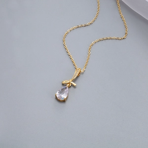 Dettaglio di una collana dorata con un grande zircone a goccia e ciondolo a fiocco