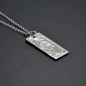 Macro shot of silver dollar sign pendant necklace featuring detailed $100 bill engraving