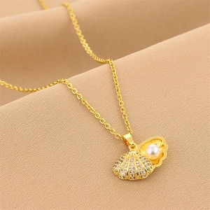 Goldene Muschelhalskette mit weißer Perle und funkelnden Kristallen auf weichem Stoff