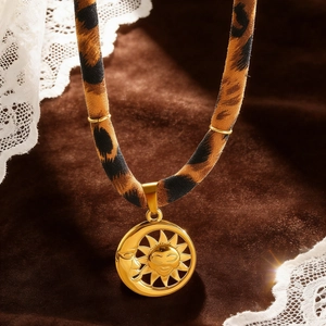 Nahaufnahme des goldenen Sonnen-Mond-Anhängers an einer Samthalskette mit Leopardenmuster