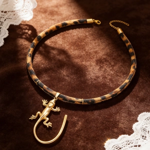 Detail eines Chokers mit Leopardenmuster und goldenem Eidechsen-Anhänger auf Samthintergrund