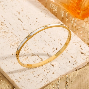 Elegant gold stainless steel bangle with white shell inlay and zircon accents on a stone base