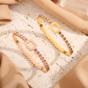 Polished gold honeycomb bangles with pink crystals on elegant neutral stone backdrop