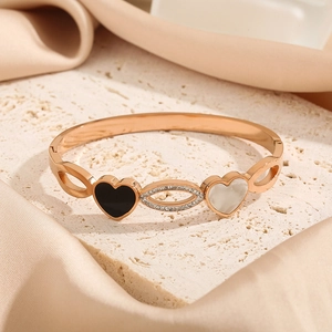 Rose gold heart bangle with black enamel and white shell inlay on a stone surface