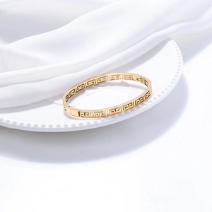 Detail of gold-plated titanium steel bangle with intricate Greek meander cutout patterns