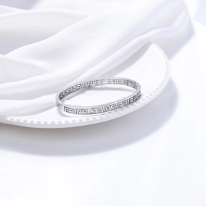 Detail shot of silver titanium steel bangle with Greek meander cutout on a white ceramic plate