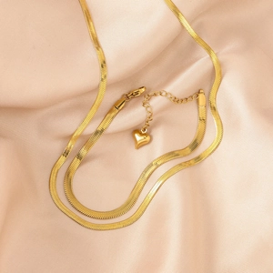 Detailed macro of gold herringbone chain with heart pendant on champagne silk