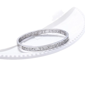 Silver stainless steel bangle featuring Greek key cutout design on a ceramic tray