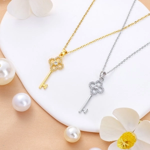 Elegant gold and silver clover key necklaces with cubic zirconia on satin background
