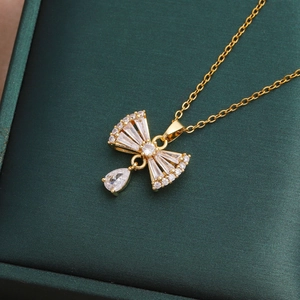 Elegante collana a fiocco dorata con zirconi e ciondolo a goccia su una scatola verde
