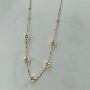 Detailed view of handmade gold chain necklace with delicate white pearl daisy flower charms