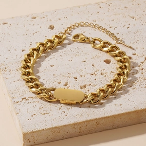 Detail of gold Cuban link chain bracelet with blank oval plate on beige stone