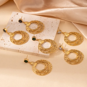 Detail of gold layered wavy hoop earrings with colorful gemstones on a stone surface