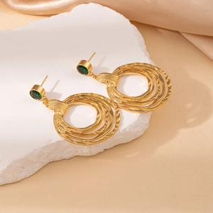 Detail of gold layered hoop earrings with green stone on white stone background