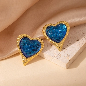 Detalle de pendientes de corazón vintage con metal martillado dorado y piedras de resina azul