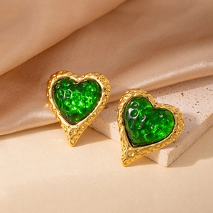 Detalle de pendientes de corazón dorados con resina verde esmeralda sobre tela de seda