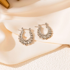 Détail de boucle d'oreille fer à cheval argentée avec texture coquillage et petit cœur