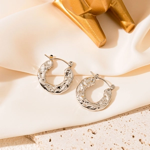Détail de boucles d'oreilles géométriques en argent avec texture martelée sur soie