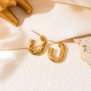 Detail view of gold U-shaped earrings with star engravings on a beige silk background