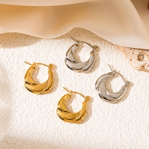 Detailed view of twisted gold and silver hoop earrings on a beige satin background