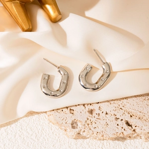 Macro detail of U-shaped silver earrings with star engravings on textured stone and silk