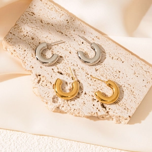 Macro detail of polished gold and silver C-shape earrings on travertine and silk texture