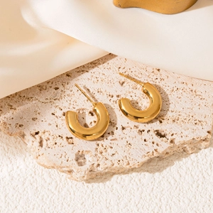 Detailed view of polished gold C-shaped earrings resting on a textured beige stone surface