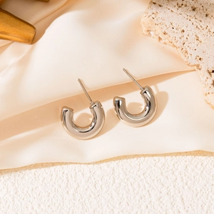 Detailed view of silver thick C-shaped stainless steel earrings on a textured stone