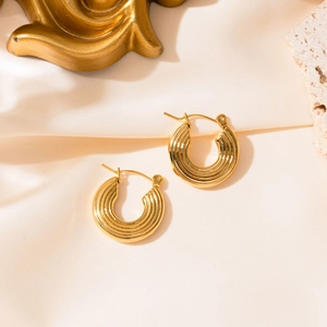 Détail macro de boucles d'oreilles créoles dorées avec texture côtelée sur soie