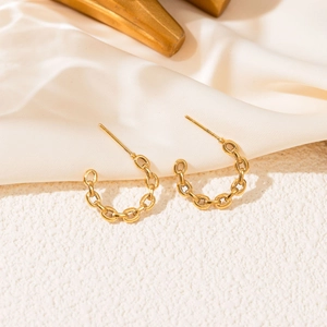 Close-up of golden chain-link C-shaped earrings on cream silk fabric texture