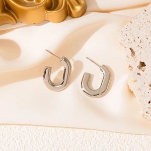 Close-up of a pair of silver U-shaped hoop earrings on elegant silk and stone backdrop