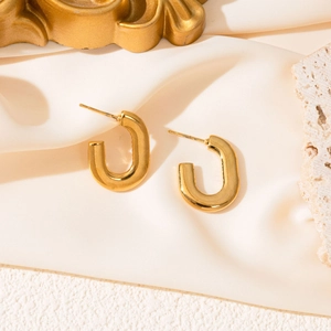 Detail view of golden U-shaped earrings on elegant silk background and stone