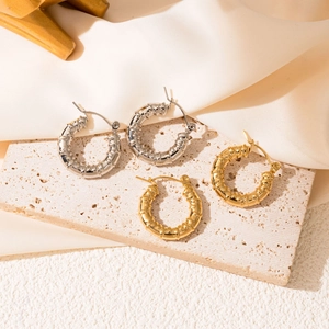 Dettaglio di orecchini a cerchio texture bambù in oro e argento su travertino