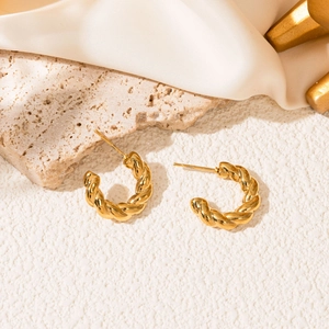Close-up of golden twist hoop earrings with high-polish finish on creamy silk and stone