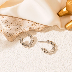 Macro shot of twisted silver hoop earrings with polished rope texture on silk background