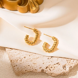 Macro detail of golden twisted C-shaped earrings on elegant textured background