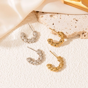 Close-up of gold and silver C-shaped earrings with embossed heart patterns on silk background