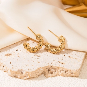 Close-up of golden C-shaped earrings with connected heart motifs on a stone display
