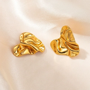 Detailopname van gouden onregelmatige geplooide oorbellen op elegante champagne zijden stof