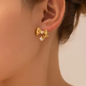Close-up of golden bow earrings with dangling white pearls and textured metallic finish