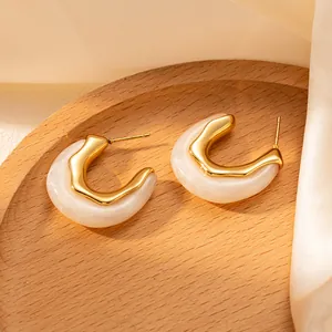 Dettaglio di eleganti orecchini a C dorati con trama marmo bianco su tessuto di seta
