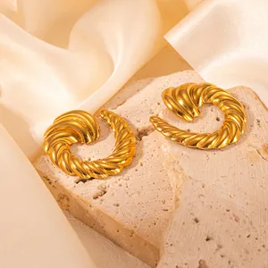 Detail von goldenen Creolen im gedrehten Croissant-Stil auf Stein und Seide