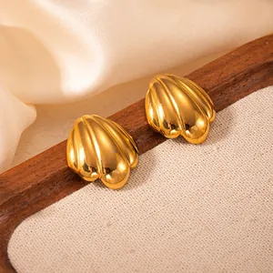 Nahaufnahme goldener Ohrstecker in Muschelform mit polierter Textur auf Seidenstoff