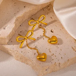 Detail shot of golden bow earrings with heart tassel on cream silk and stone base
