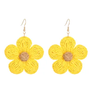 Macro detail of hand-woven yellow raffia sunflower earrings with gold metal hooks