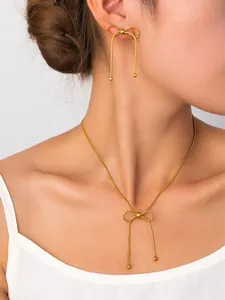 Dettaglio del set di collana e orecchini con fiocco dorato e nappe indossato dal modello