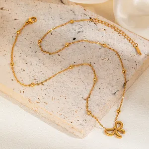 Detailed close-up of a golden bow pendant necklace with bead chain on stone and silk