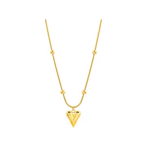 Détail du collier chaîne serpent dorée avec perles et pendentif coeur sur fond blanc pur